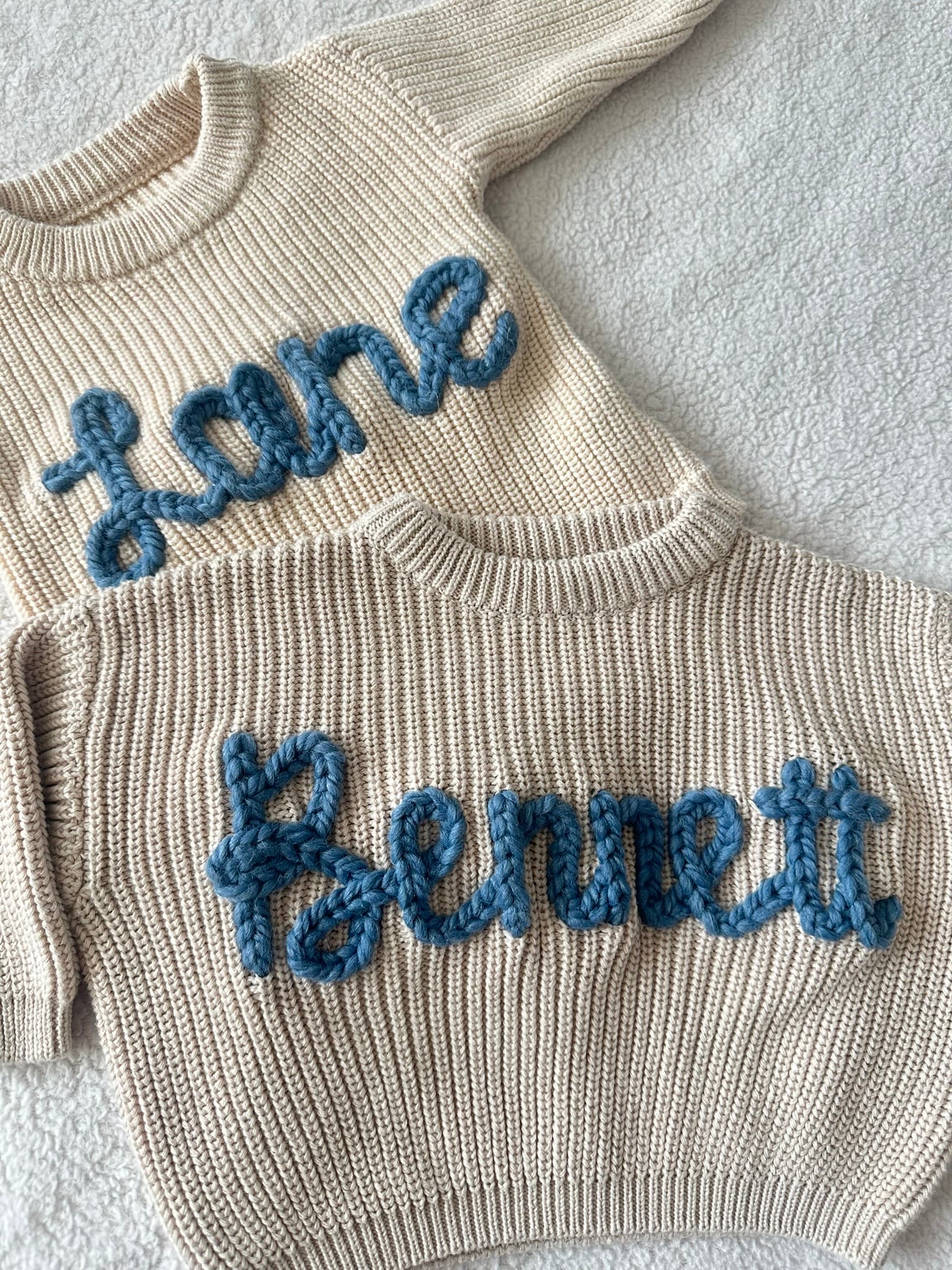 Two cream sweaters stitched with the names Lane and Bennett in blue