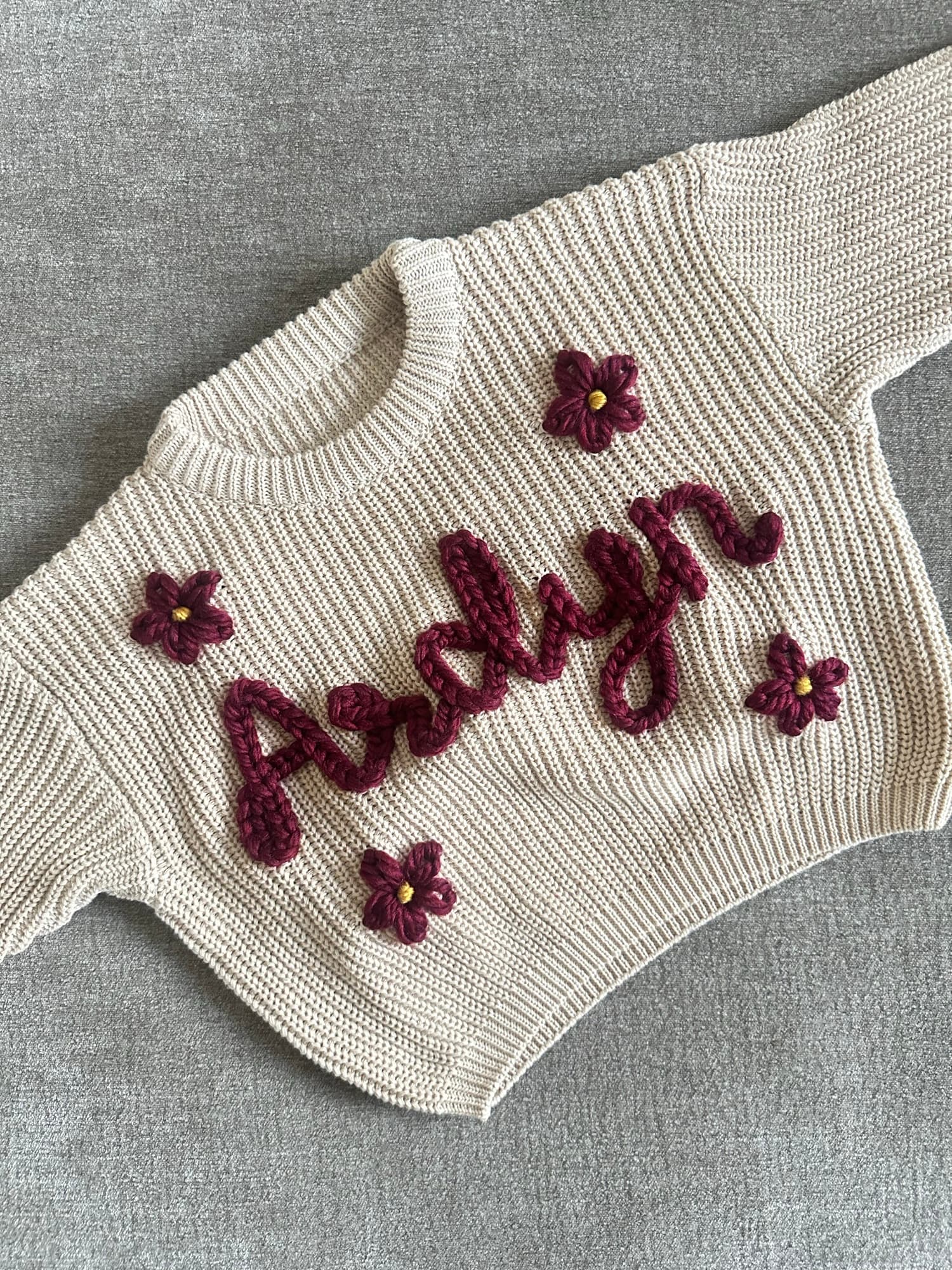 Cream sweater stitched with the name Ardyn in burgundy with small crochet flowers