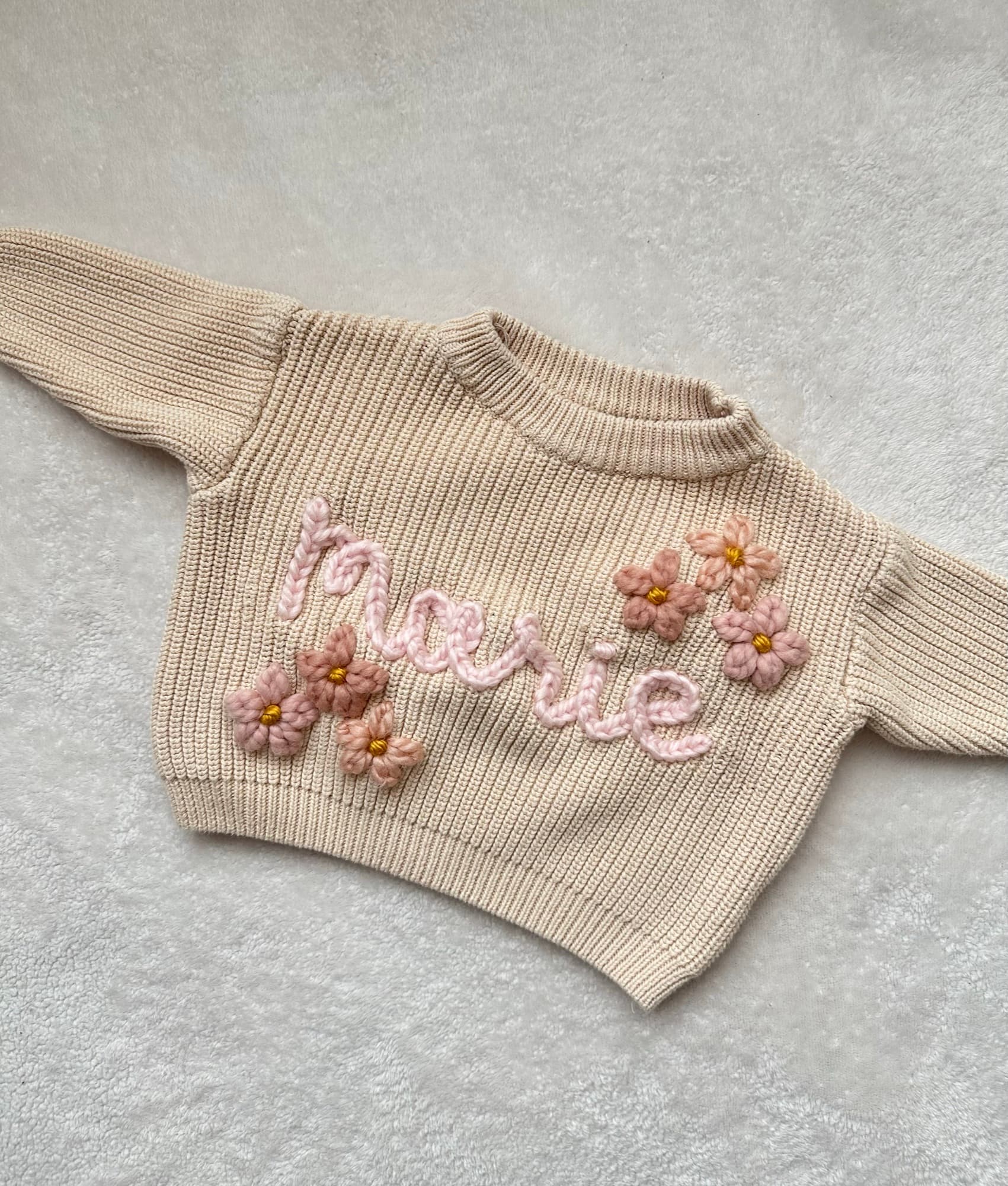 Beige sweater stitched with the name Marie in pink with crochet flowers